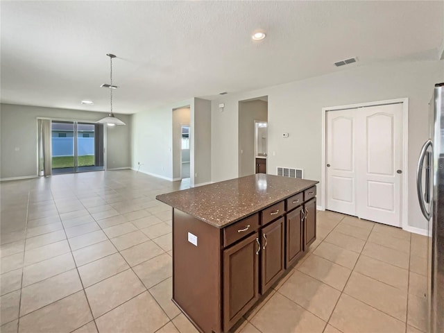 2587 Isabela Ter, Kissimmee, FL 34743 - kitchen with light tile patterned floors, a center island, freestanding refrigerator, dark stone counters, and open floor plan