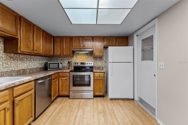 1384 La Paloma Cir, Winter Springs, FL 32708 - kitchen with stainless steel appliances, under cabinet range hood, light wood-style flooring, tasteful backsplash, and brown cabinetry