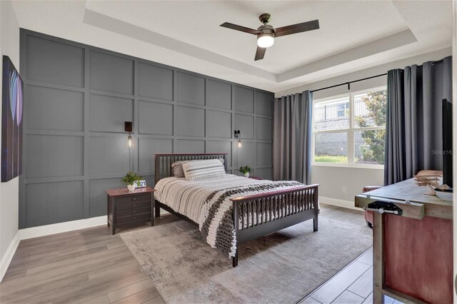 1219 Foltz Loop, Oakland, FL 34787 - bedroom featuring a decorative wall, a tray ceiling, light wood finished floors, and a ceiling fan