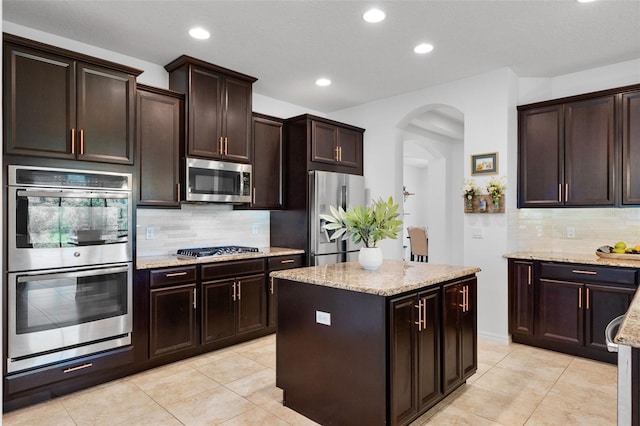 13851 Jomatt Loop, Winter Garden, FL 34787 - kitchen with appliances with stainless steel finishes, arched walkways, decorative backsplash, light stone counters, and light tile patterned floors