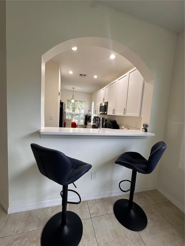 10110 SW Chadwick Dr, Port St Lucie, FL 34987 - kitchen featuring stainless steel microwave, freestanding refrigerator, a kitchen bar, arched walkways, and light countertops