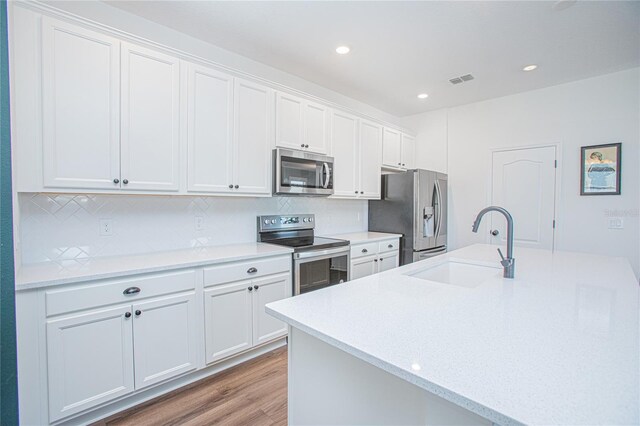 786 Steerview St, Saint Cloud, FL 34771 - kitchen with stainless steel appliances, light wood finished floors, tasteful backsplash, white cabinetry, and a kitchen island with sink