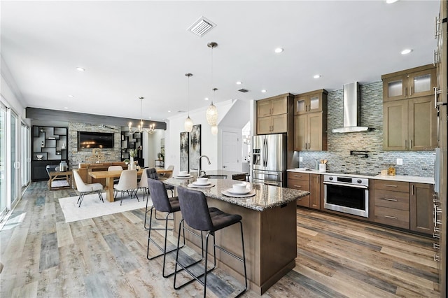 15350 Arabian Way, Montverde, FL 34756 - kitchen with stainless steel appliances, wall chimney exhaust hood, a chandelier, a breakfast bar area, and light wood-style flooring