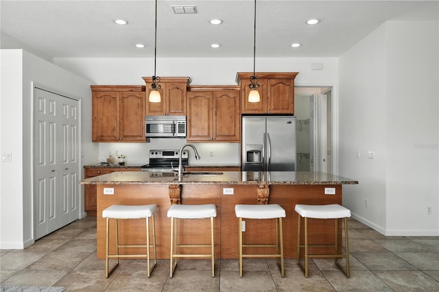 15350 Arabian Way, Montverde, FL 34756 - kitchen with appliances with stainless steel finishes, an island with sink, brown cabinets, dark stone counters, and a breakfast bar