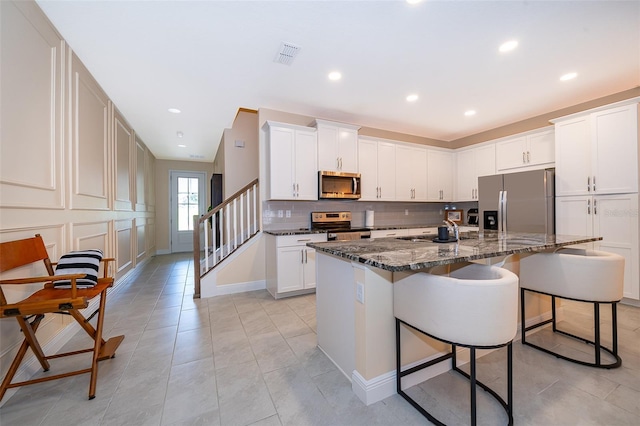 1660 Tropical Palms Cir, Kissimmee, FL 34747 - kitchen with appliances with stainless steel finishes, a breakfast bar, decorative backsplash, dark stone counters, and a center island with sink