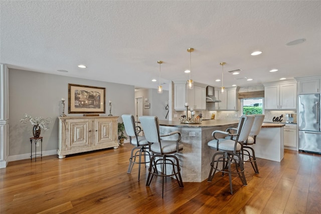 9070 Ron Den Ln, Windermere, FL 34786 - kitchen featuring stainless steel refrigerator, wall chimney exhaust hood, a kitchen breakfast bar, wood finished floors, and a textured ceiling