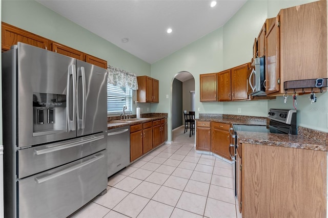 1041 Mccully Ct, Oviedo, FL 32765 - kitchen with stainless steel appliances, arched walkways, light tile patterned floors, brown cabinets, and lofted ceiling