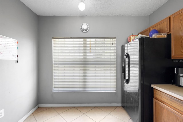 1040 Cannock Dr, Kissimmee, FL 34758 - kitchen featuring freestanding refrigerator, a textured ceiling, brown cabinets, light tile patterned flooring, and light countertops