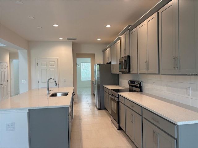 7260 Dilly Lake Ave, Groveland, FL 34736 - kitchen featuring appliances with stainless steel finishes, gray cabinets, a center island with sink, backsplash, and light countertops