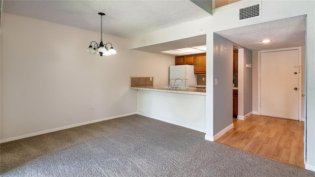 6019 Windhover Dr Unit C10-2, Orlando, FL 32819 - kitchen with a textured ceiling, light colored carpet, a chandelier, freestanding refrigerator, and pendant lighting