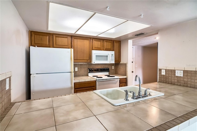 6019 Windhover Dr Unit C10-2, Orlando, FL 32819 - kitchen featuring white appliances, tile countertops, brown cabinetry, and backsplash
