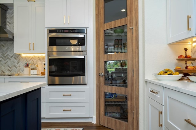 13235 Vennetta Way, Windermere, FL 34786 - kitchen with stainless steel double oven, backsplash, wall chimney range hood, and white cabinetry
