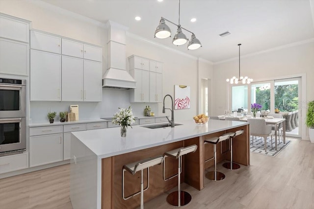 17 Old Oak Dr N, Palm Coast, FL 32137 - kitchen featuring stainless steel double oven, light wood-style flooring, custom range hood, crown molding, and light countertops