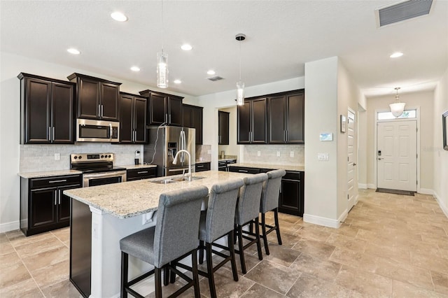 1833 Benoit Ter, Davenport, FL 33837 - kitchen featuring appliances with stainless steel finishes, decorative backsplash, a kitchen bar, a kitchen island with sink, and hanging light fixtures