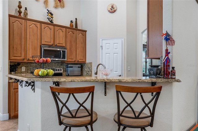 859 Leather Fern Ln, Mims, FL 32754 - kitchen featuring stainless steel microwave, a kitchen bar, tasteful backsplash, and brown cabinets