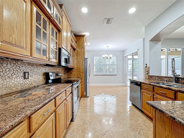 229 Largovista Dr, Oakland, FL 34787 - kitchen with appliances with stainless steel finishes, decorative backsplash, a chandelier, brown cabinetry, and dark stone counters