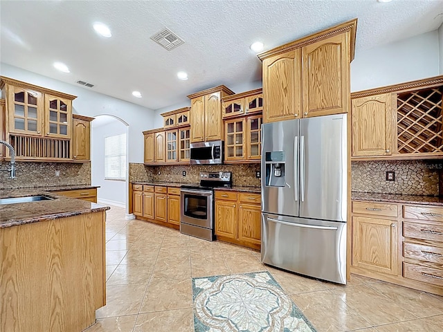 229 Largovista Dr, Oakland, FL 34787 - kitchen with appliances with stainless steel finishes, backsplash, dark stone counters, arched walkways, and glass insert cabinets