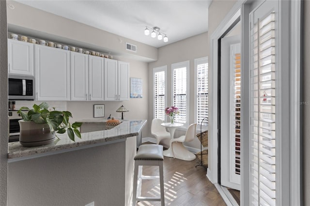 501 Mirasol Cir Unit 304, Kissimmee, FL 34747 - kitchen featuring stainless steel microwave, light stone countertops, white cabinets, wood finished floors, and a breakfast bar area