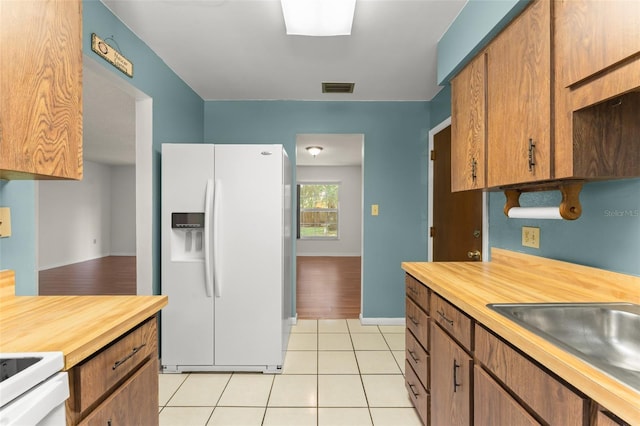 17 Rosewood Dr, Davenport, FL 33837 - kitchen with white refrigerator with ice dispenser, range, butcher block counters, light tile patterned floors, and brown cabinetry