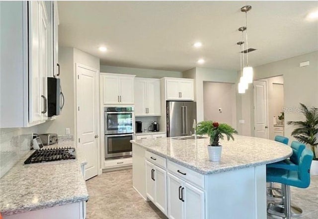 13542 Gorgona Isle Dr, Windermere, FL 34786 - kitchen featuring appliances with stainless steel finishes, a kitchen bar, white cabinetry, an island with sink, and decorative light fixtures