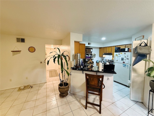 4690 Sussex Ter Unit 103, Orlando, FL 32811 - kitchen featuring freestanding refrigerator, a peninsula, dark countertops, brown cabinetry, and light tile patterned flooring