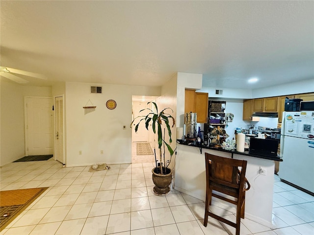 4690 Sussex Ter Unit 103, Orlando, FL 32811 - kitchen featuring freestanding refrigerator, dark countertops, a peninsula, brown cabinets, and light tile patterned floors