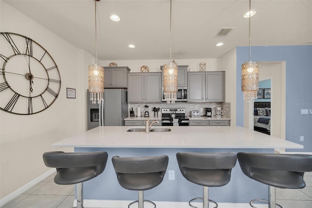 8940 Zurich Ln, Kissimmee, FL 34747 - kitchen with appliances with stainless steel finishes, gray cabinets, light countertops, a kitchen island with sink, and a breakfast bar area