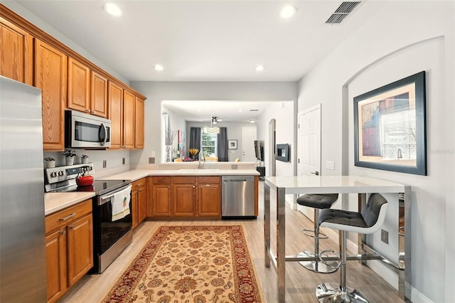 14241 Confetti Dr, Windermere, FL 34786 - kitchen with appliances with stainless steel finishes, a peninsula, light wood-style flooring, brown cabinetry, and recessed lighting