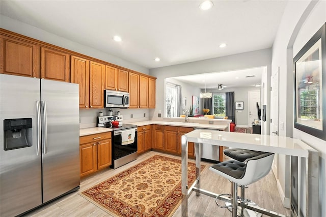 14241 Confetti Dr, Windermere, FL 34786 - kitchen with stainless steel appliances, a peninsula, light wood-style flooring, light countertops, and brown cabinets