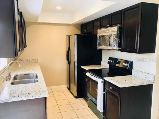 3370 Cedar Springs Pl Unit 156, Winter Park, FL 32792 - kitchen with black appliances, a raised ceiling, light tile patterned floors, light stone countertops, and dark cabinets