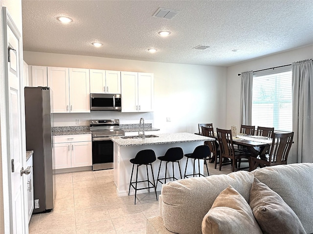 764 Richmond Estate Ave, Haines City, FL 33844 - kitchen with stainless steel appliances, open floor plan, a kitchen bar, white cabinetry, and a textured ceiling