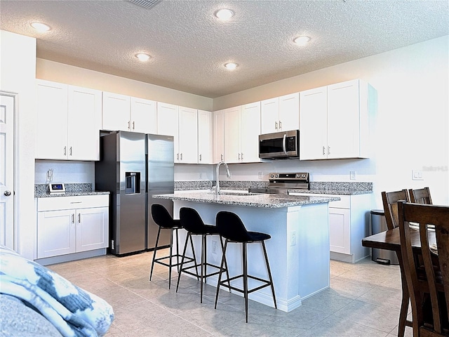 764 Richmond Estate Ave, Haines City, FL 33844 - kitchen with stainless steel appliances, a kitchen breakfast bar, an island with sink, white cabinets, and a textured ceiling