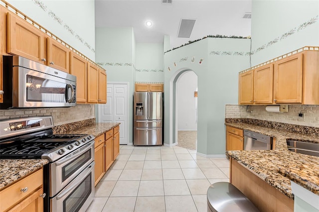 12617 Douglas Fir Ct, Clermont, FL 34711 - kitchen featuring appliances with stainless steel finishes, a high ceiling, arched walkways, stone counters, and light tile patterned floors