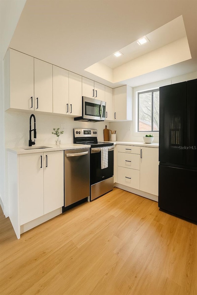 1050 E Michigan St Unit 1050B, Orlando, FL 32806 - kitchen with stainless steel appliances, light wood-style flooring, light countertops, a raised ceiling, and white cabinetry