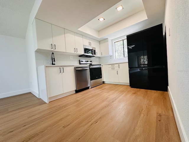1050 E Michigan St Unit 1050B, Orlando, FL 32806 - kitchen featuring appliances with stainless steel finishes, a tray ceiling, light wood-type flooring, white cabinetry, and light countertops