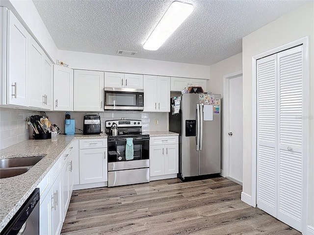 745 Mentmore Cir, Deltona, FL 32738 - kitchen featuring appliances with stainless steel finishes, a textured ceiling, light wood finished floors, white cabinets, and backsplash