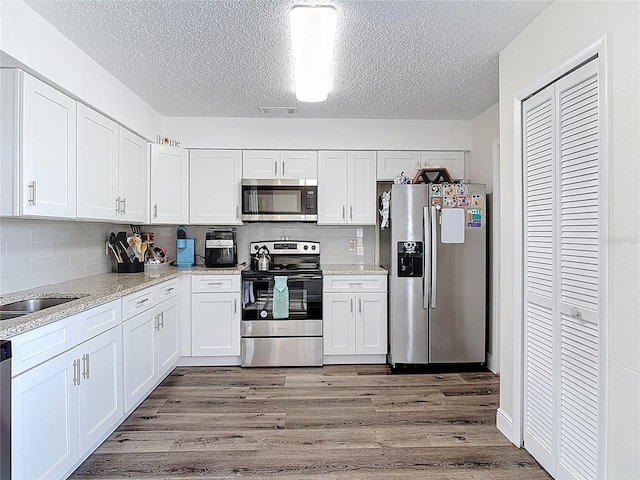 745 Mentmore Cir, Deltona, FL 32738 - kitchen featuring stainless steel appliances, a textured ceiling, wood finished floors, white cabinetry, and backsplash