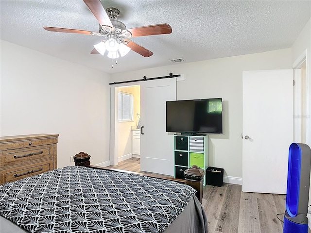 745 Mentmore Cir, Deltona, FL 32738 - bedroom with light wood-style flooring, a barn door, a textured ceiling, a ceiling fan, and connected bathroom