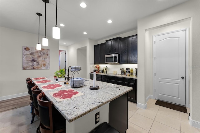 4920 Blanche Ct, Saint Cloud, FL 34772 - kitchen with light stone countertops, light tile patterned floors, an island with sink, dark cabinetry, and a breakfast bar