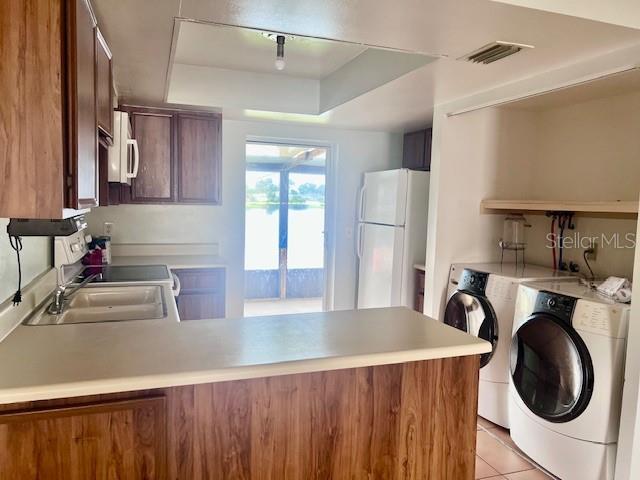 19 W Country Cove Way, Kissimmee, FL 34743 - kitchen featuring white appliances, independent washer and dryer, a peninsula, a raised ceiling, and light countertops
