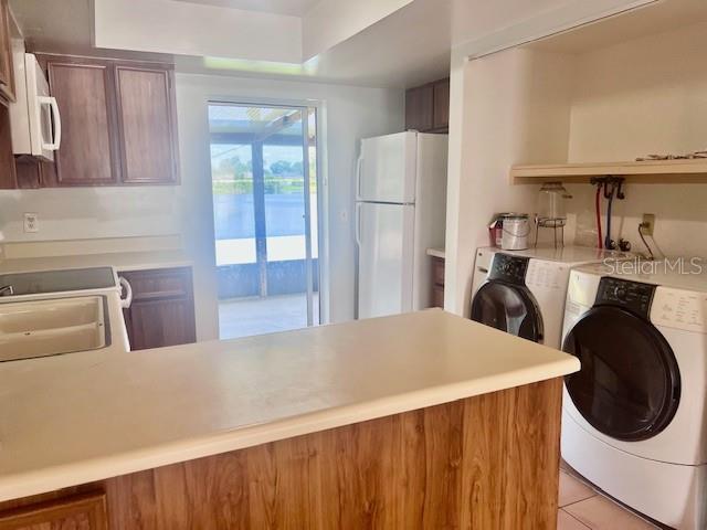19 W Country Cove Way, Kissimmee, FL 34743 - kitchen featuring white appliances, washer and clothes dryer, light tile patterned flooring, a peninsula, and light countertops