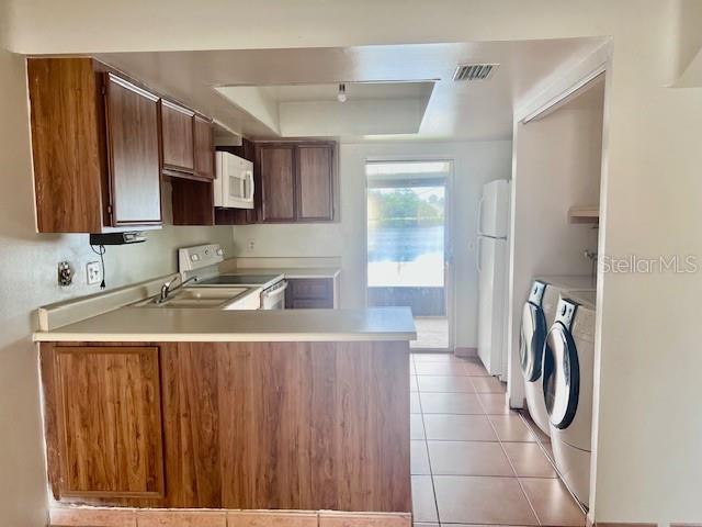 19 W Country Cove Way, Kissimmee, FL 34743 - kitchen with washing machine and dryer, white appliances, a raised ceiling, a peninsula, and light countertops