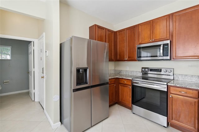 6059 Twain St Unit 108, Orlando, FL 32835 - kitchen with stainless steel appliances, light tile patterned floors, brown cabinets, and light stone counters