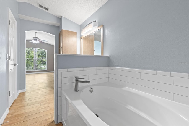 3245 Kings Ridge Ter, Deltona, FL 32725 - bathroom featuring vaulted ceiling, a bath, wood finished floors, a textured ceiling, and ceiling fan
