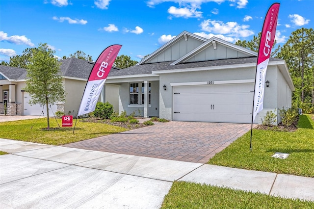 1261 Champions Dr, Daytona Beach, FL 32124 - ranch-style house with decorative driveway, a garage, a front lawn, board and batten siding, and roof with shingles