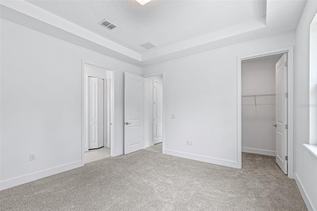 1261 Champions Dr, Daytona Beach, FL 32124 - unfurnished bedroom with light carpet, a tray ceiling, a textured ceiling, and a walk in closet