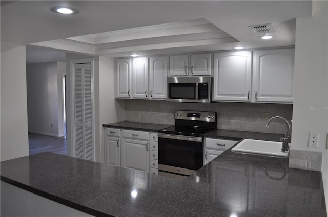 721 Elkhorn Rd, Sun City Center, FL 33573 - kitchen featuring stainless steel appliances, dark countertops, a raised ceiling, white cabinetry, and crown molding