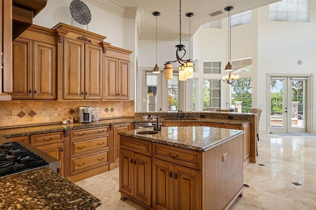 11209 Macaw Ct, Windermere, FL 34786 - kitchen featuring ornamental molding, brown cabinets, tasteful backsplash, dark stone countertops, and an island with sink