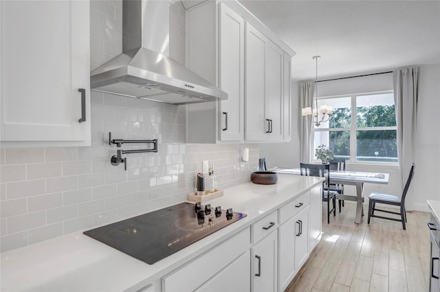 4477 Renly Ln, Clermont, FL 34711 - kitchen featuring wall chimney exhaust hood, black electric stovetop, a chandelier, tasteful backsplash, and white cabinetry