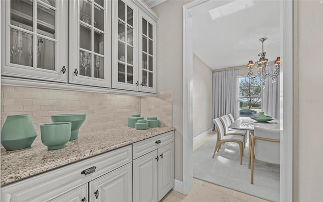 12023 Gold Creek Trl, Windermere, FL 34786 - kitchen with a chandelier, glass insert cabinets, backsplash, light stone countertops, and white cabinetry